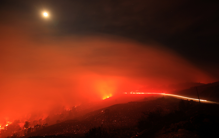 The Rocky Fire burns up and over a ridge underneath a full moon along Morgan Valley Road early Thursday morning  July 30, 2015.  The fire has grown to 8,000 acres since yesterday afternoon.  Lights from a strike team of engines can be seen on the right hand side in this long exposure. (Kent Porter / Press Democrat) 2015